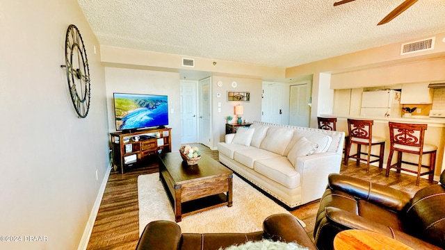 living room featuring hardwood / wood-style floors, ceiling fan, and a textured ceiling