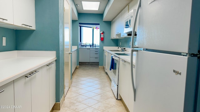 kitchen with white appliances, light tile patterned floors, sink, white cabinets, and a skylight