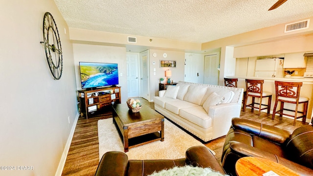 living room featuring hardwood / wood-style flooring, ceiling fan, and a textured ceiling