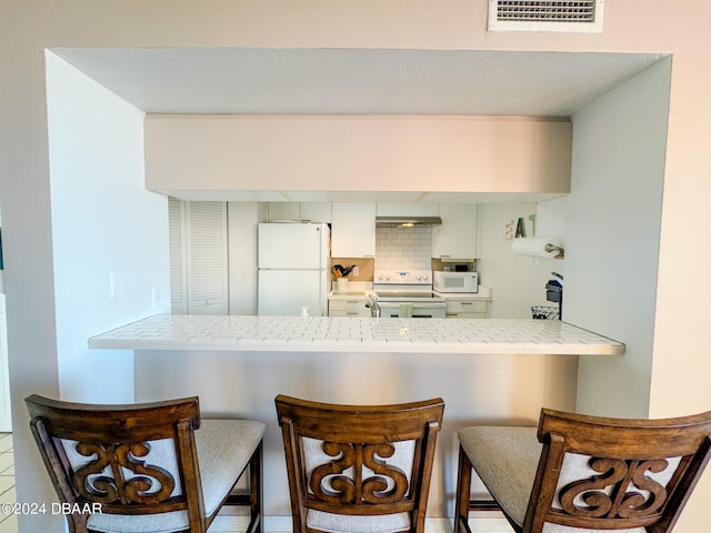 kitchen with tasteful backsplash, kitchen peninsula, white appliances, and a breakfast bar area