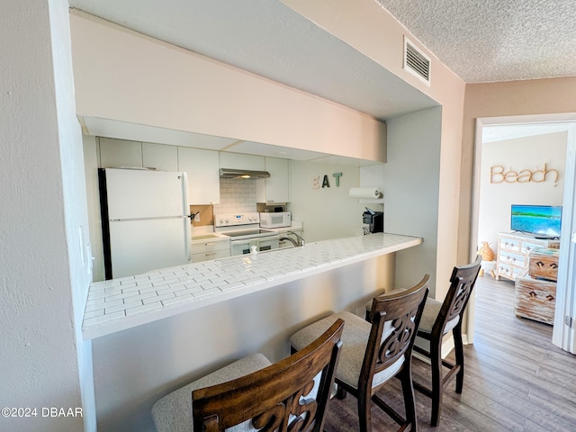 kitchen featuring white appliances, decorative backsplash, light hardwood / wood-style floors, a breakfast bar area, and kitchen peninsula