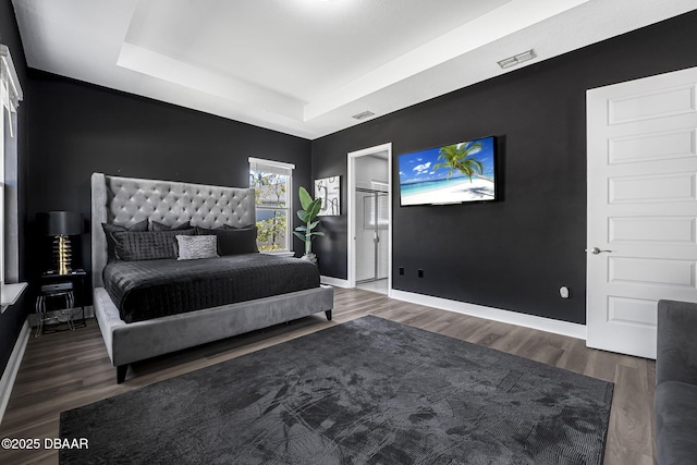 bedroom with a raised ceiling, visible vents, baseboards, and wood finished floors