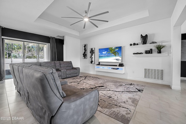 living area featuring a tray ceiling, visible vents, ceiling fan, and baseboards