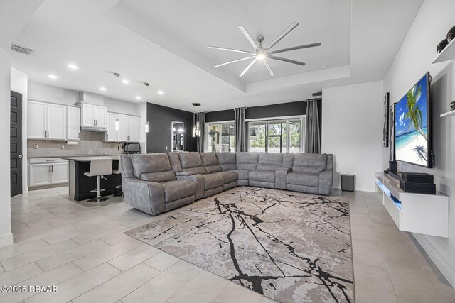 living area featuring ceiling fan, recessed lighting, visible vents, baseboards, and a raised ceiling