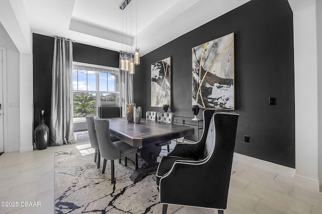 dining room featuring a tray ceiling, light tile patterned flooring, and baseboards