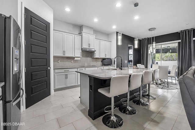 kitchen with tasteful backsplash, stainless steel fridge with ice dispenser, a sink, under cabinet range hood, and a kitchen breakfast bar