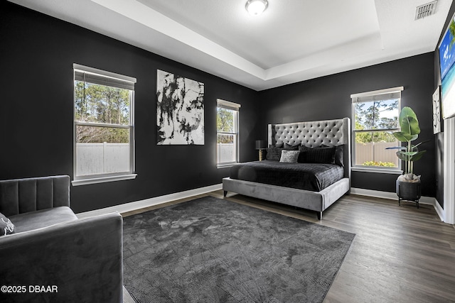 bedroom with wood finished floors, visible vents, baseboards, multiple windows, and a raised ceiling