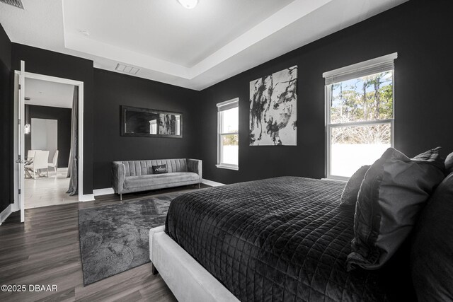 bedroom featuring a raised ceiling, visible vents, baseboards, and wood finished floors