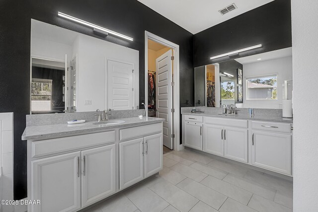 full bathroom featuring a walk in closet, visible vents, two vanities, and a sink