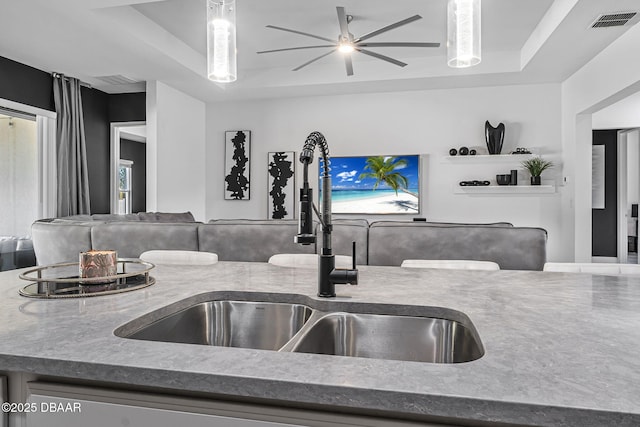 kitchen with a ceiling fan, visible vents, a tray ceiling, and a sink