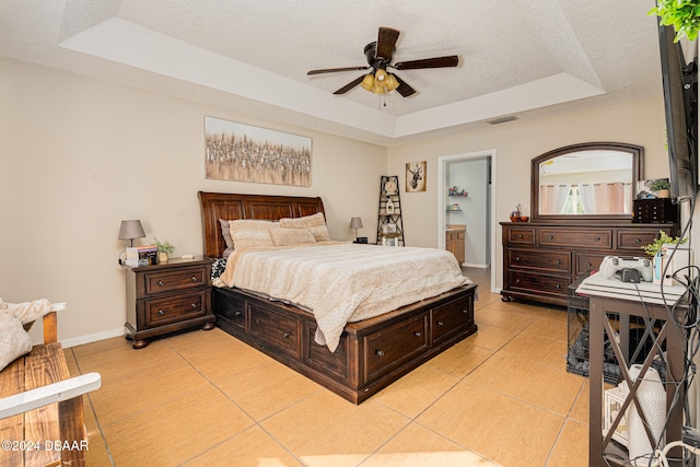 tiled bedroom featuring ensuite bath, ceiling fan, a textured ceiling, and a raised ceiling