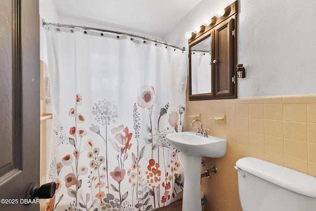 full bath with curtained shower, wainscoting, toilet, and tile walls