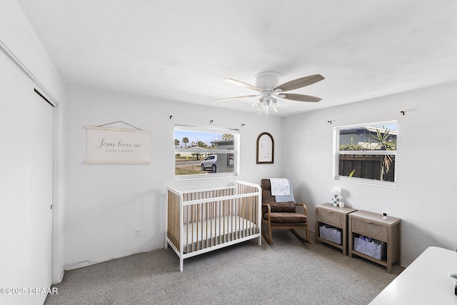 carpeted bedroom with a crib, multiple windows, a ceiling fan, and a closet