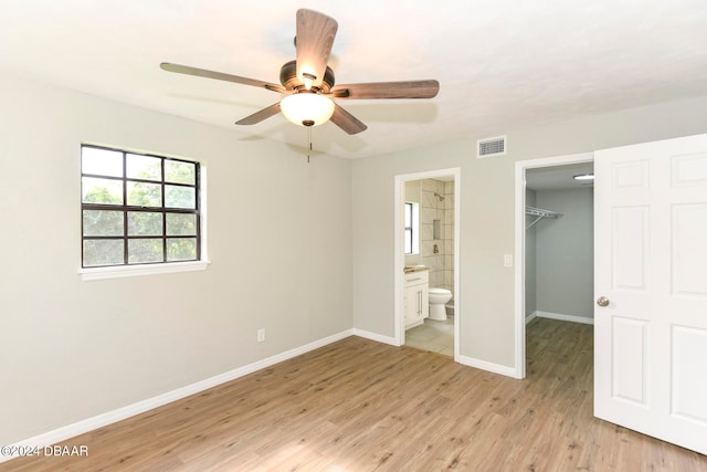 unfurnished bedroom with a closet, a spacious closet, light hardwood / wood-style flooring, ceiling fan, and ensuite bathroom