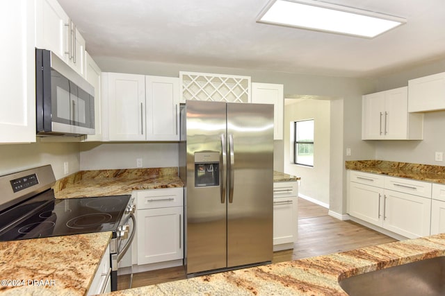 kitchen with light wood-type flooring, appliances with stainless steel finishes, light stone counters, and white cabinets