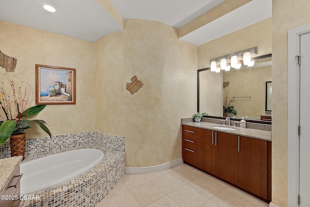 bathroom with a textured wall, vanity, tile patterned flooring, baseboards, and a bath