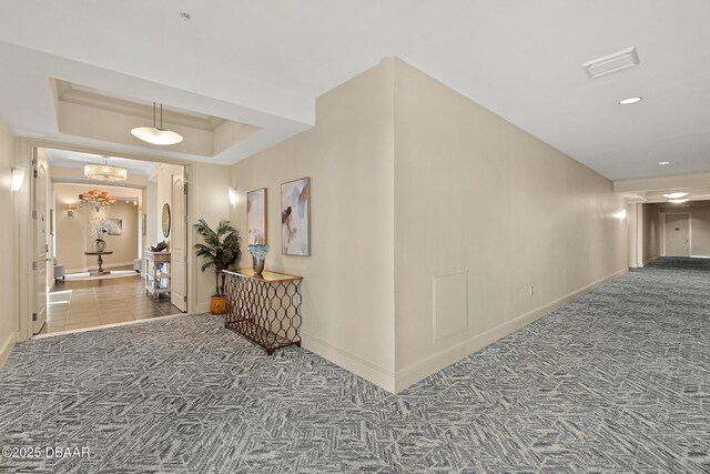 corridor featuring a tray ceiling, recessed lighting, visible vents, carpet flooring, and baseboards