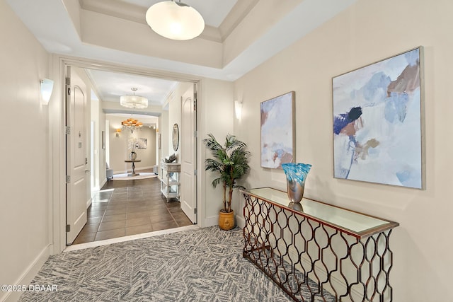 corridor featuring a raised ceiling, carpet flooring, crown molding, and an inviting chandelier