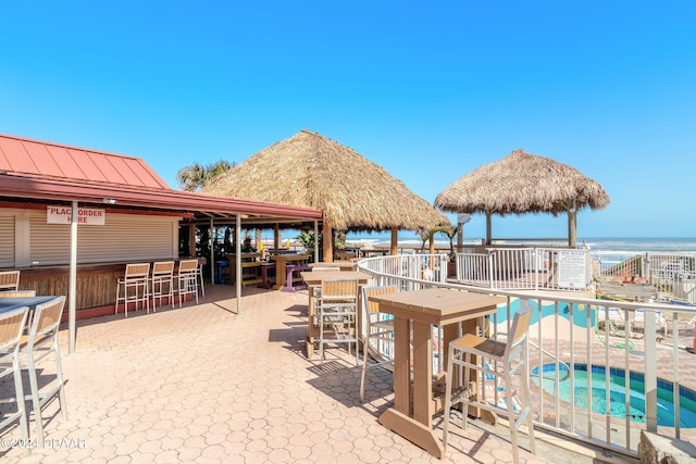 view of patio featuring exterior bar, a swimming pool with hot tub, a water view, and a gazebo