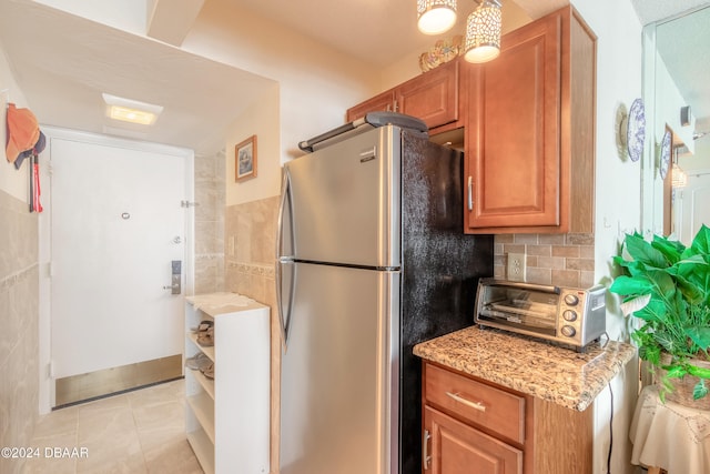 kitchen featuring light stone countertops, stainless steel refrigerator, light tile patterned floors, and tasteful backsplash