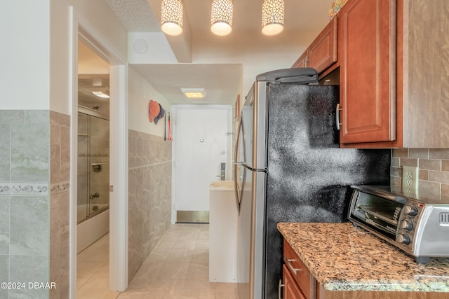 kitchen with light stone countertops, stainless steel fridge, light tile patterned floors, and tile walls