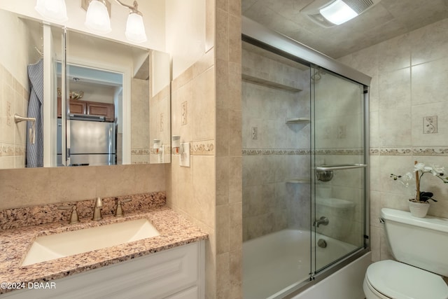 full bathroom featuring shower / bath combination with glass door, vanity, toilet, and tile walls