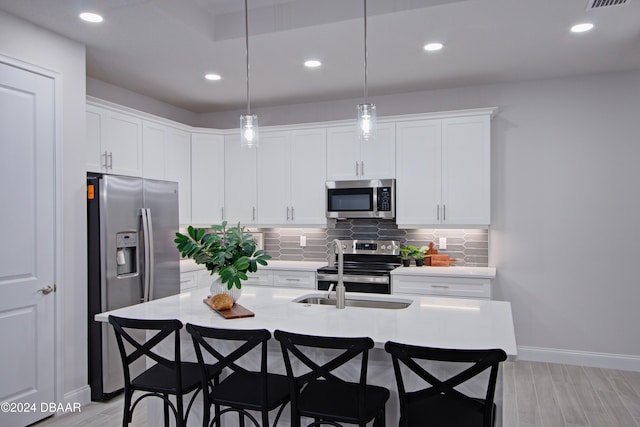 kitchen featuring stainless steel appliances, a kitchen island with sink, light hardwood / wood-style flooring, white cabinets, and hanging light fixtures