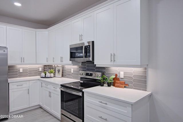 kitchen featuring decorative backsplash, white cabinetry, light wood-type flooring, and appliances with stainless steel finishes