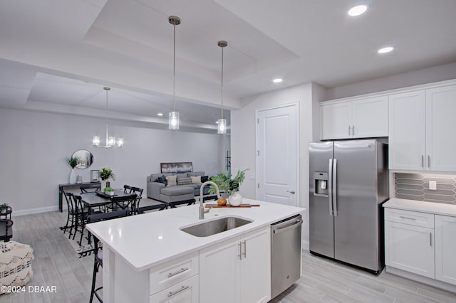 kitchen featuring white cabinetry, sink, an island with sink, decorative light fixtures, and appliances with stainless steel finishes