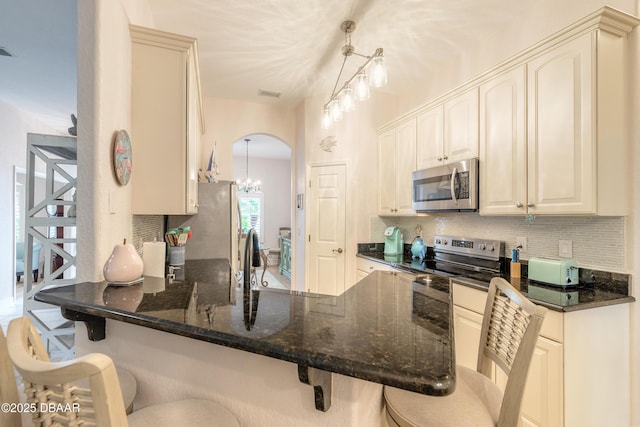 kitchen with appliances with stainless steel finishes, kitchen peninsula, a kitchen breakfast bar, and decorative light fixtures