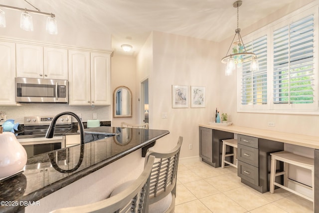 kitchen with appliances with stainless steel finishes, light tile patterned floors, hanging light fixtures, and dark stone counters