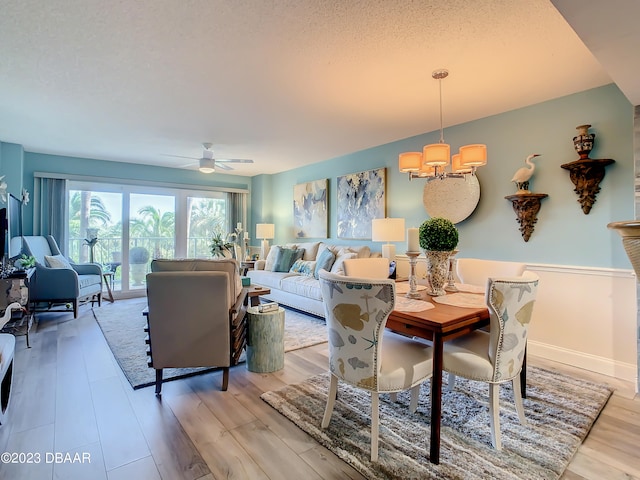 dining room with ceiling fan with notable chandelier, a textured ceiling, and light hardwood / wood-style flooring