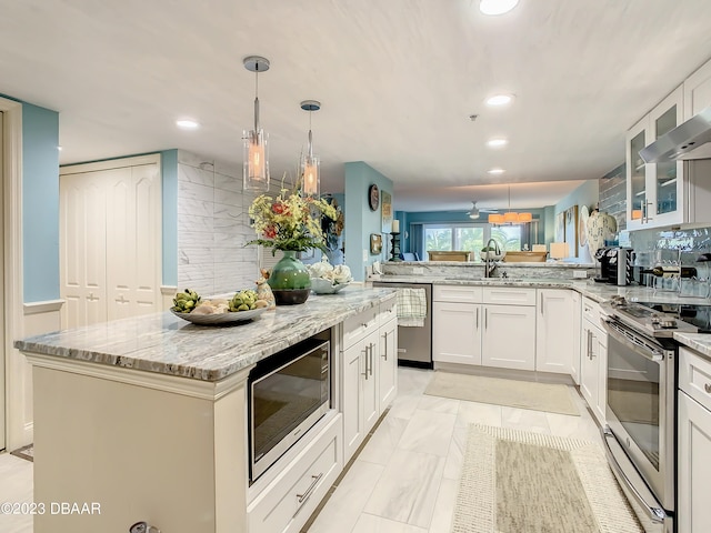 kitchen with a center island, white cabinets, kitchen peninsula, appliances with stainless steel finishes, and decorative light fixtures