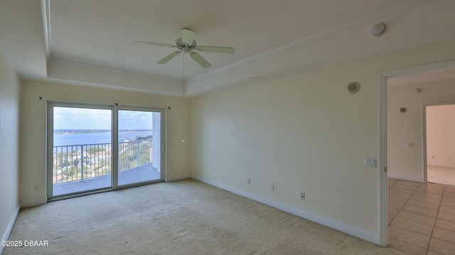 carpeted empty room with a water view, ceiling fan, ornamental molding, and a tray ceiling