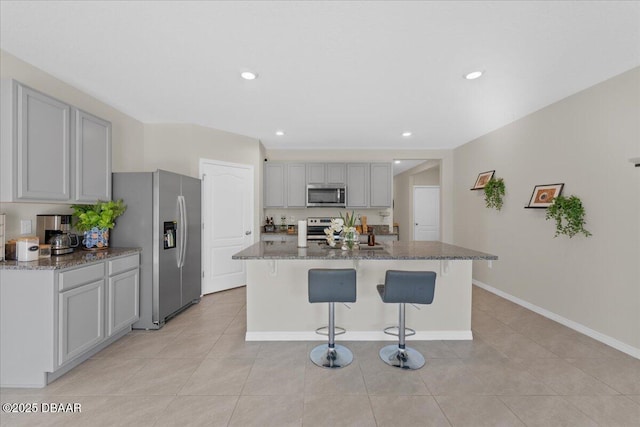 kitchen with gray cabinetry, a center island with sink, a kitchen breakfast bar, appliances with stainless steel finishes, and light tile patterned flooring