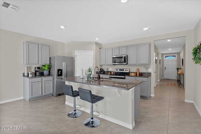 kitchen featuring appliances with stainless steel finishes, a kitchen island with sink, gray cabinetry, and sink