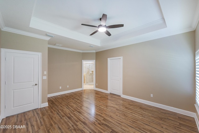 empty room with crown molding, wood finished floors, baseboards, ceiling fan, and a raised ceiling