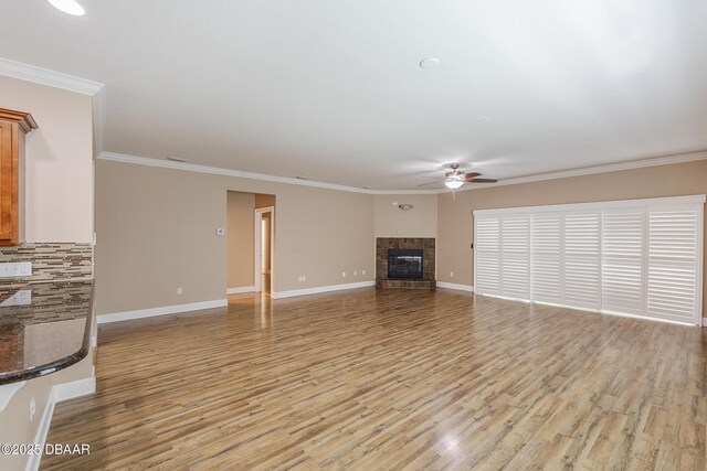 unfurnished living room featuring crown molding, baseboards, ceiling fan, light wood-type flooring, and a tile fireplace