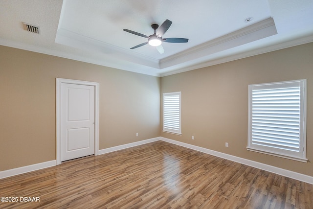 unfurnished room with visible vents, ornamental molding, wood finished floors, and a raised ceiling