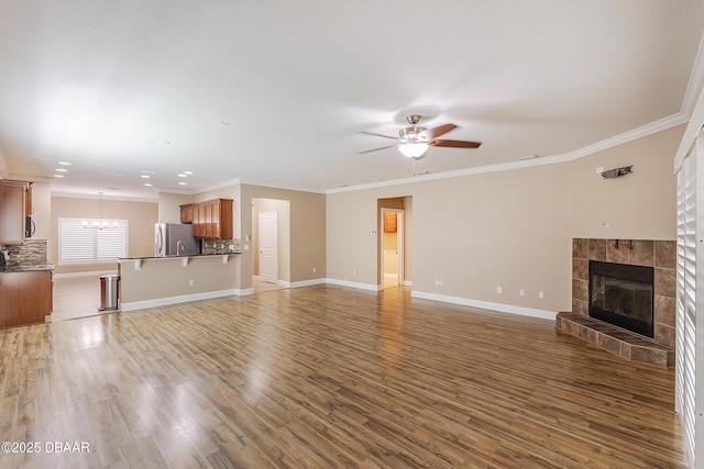 unfurnished living room featuring light wood-style floors, ornamental molding, ceiling fan with notable chandelier, and a fireplace