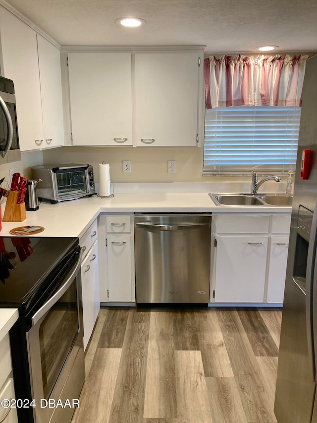 kitchen with white cabinets, light hardwood / wood-style floors, appliances with stainless steel finishes, and sink