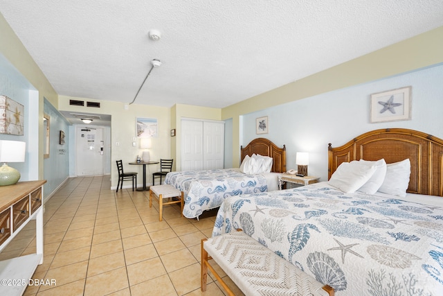 bedroom featuring light tile patterned floors, visible vents, a closet, and a textured ceiling