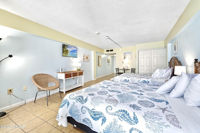 bedroom featuring light tile patterned floors, baseboards, visible vents, a closet, and a textured ceiling