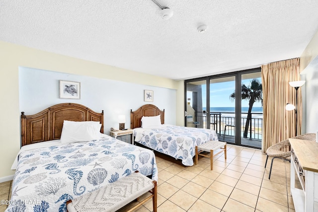 bedroom featuring a water view, access to outside, a textured ceiling, a wall of windows, and light tile patterned floors