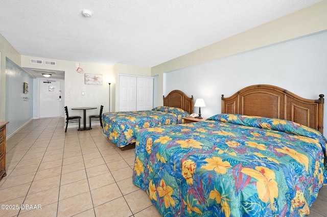 bedroom featuring light tile patterned floors, a textured ceiling, visible vents, baseboards, and a closet