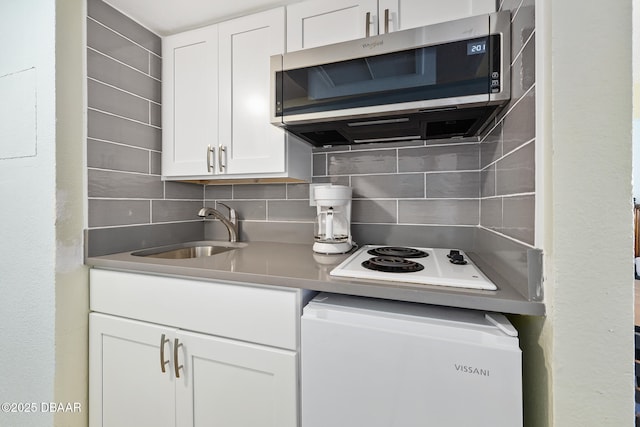 kitchen featuring white electric stovetop, a sink, white cabinets, stainless steel microwave, and tasteful backsplash