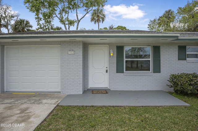 doorway to property featuring brick siding, an attached garage, and concrete driveway