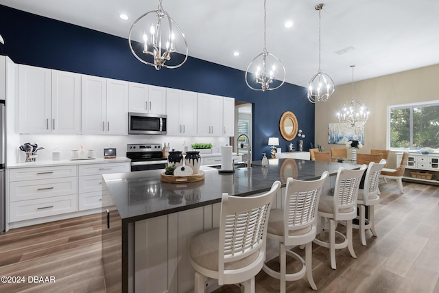 kitchen with white cabinetry, hanging light fixtures, wood-type flooring, a center island with sink, and appliances with stainless steel finishes