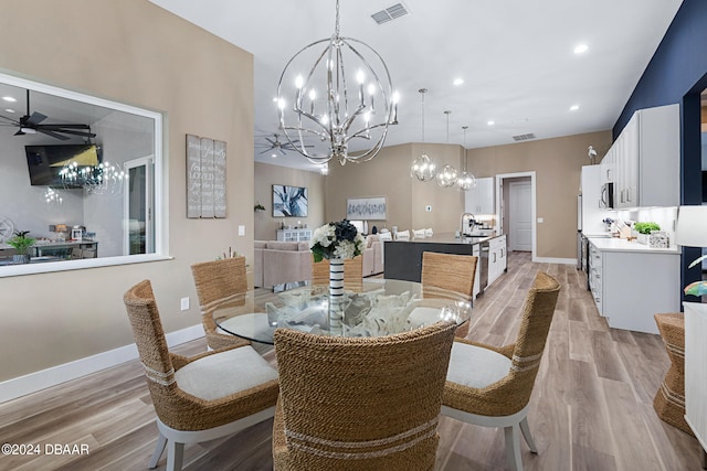 dining space with ceiling fan with notable chandelier, sink, and light hardwood / wood-style flooring