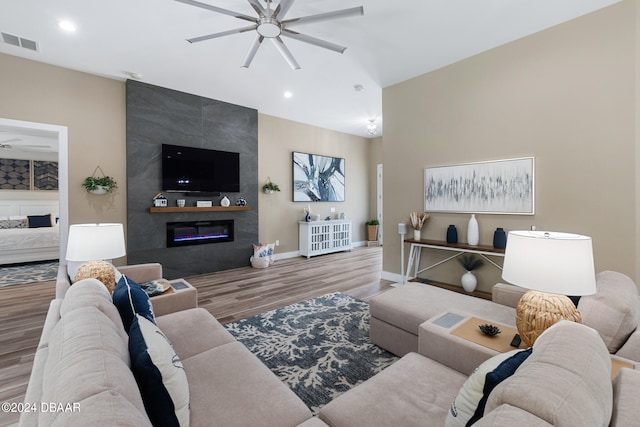 living room with hardwood / wood-style flooring, ceiling fan, and a tiled fireplace